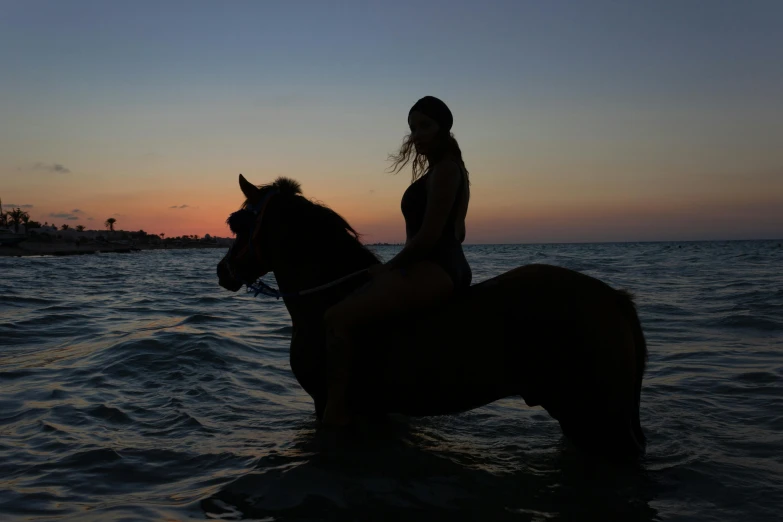 girl sitting on a horse in water at sunset