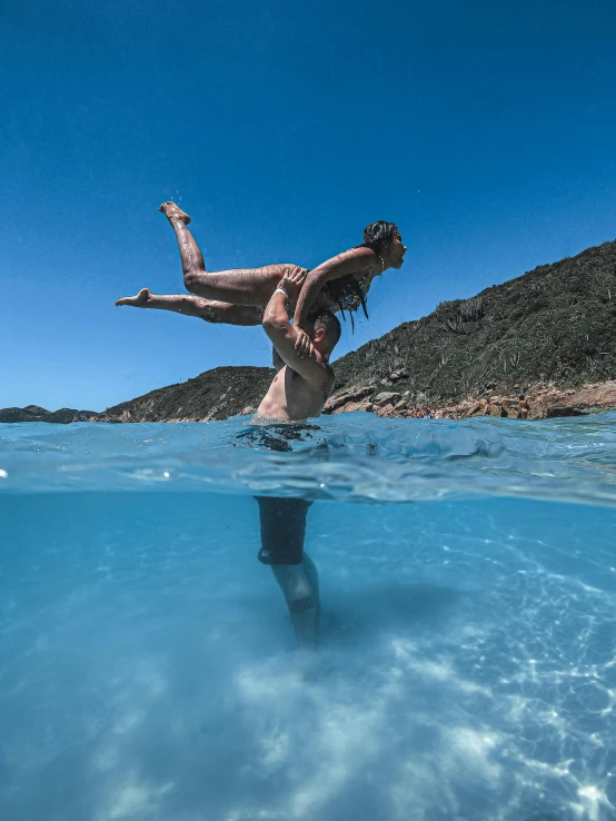 woman standing in clear water as she dives with back to camera