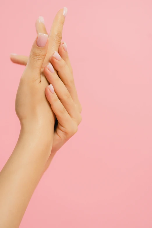 the woman's hands are holding her nails while against a pink background