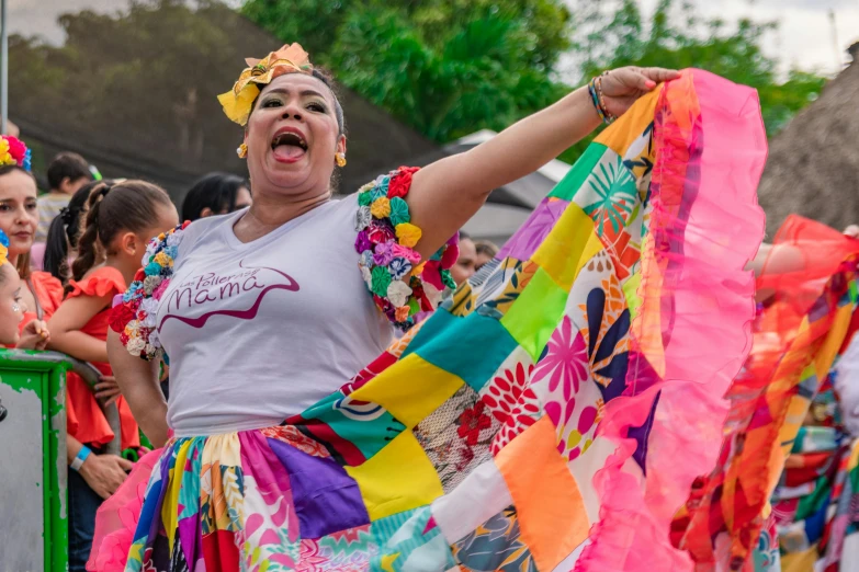 a woman in a colorful dress holds out a colorful sheet while people watch