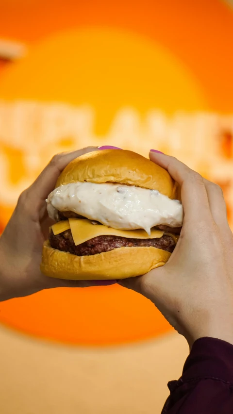 a person holding onto a big hamburger near a sign