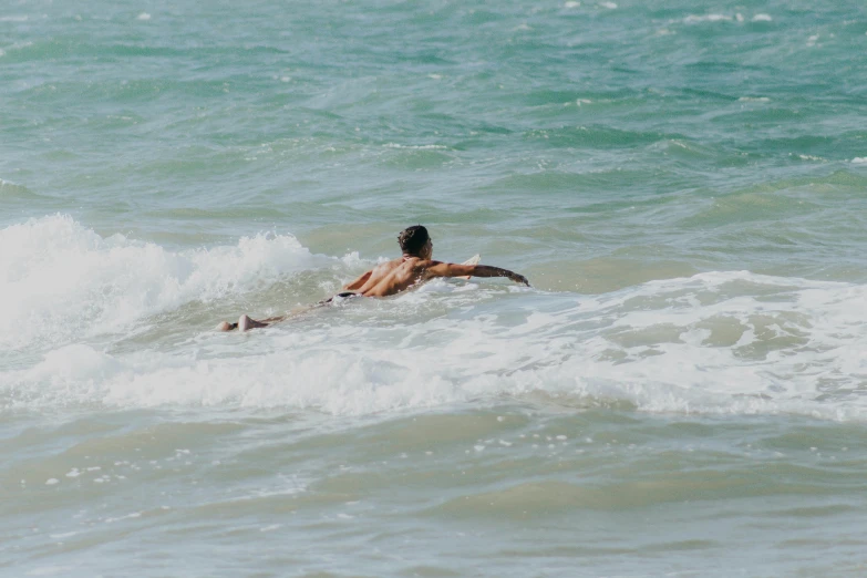 person lying down in the ocean surfing on his surfboard