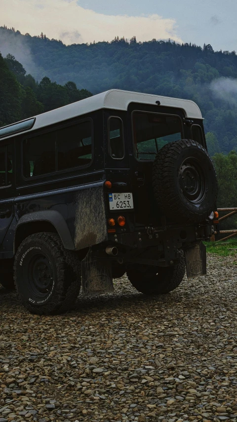 a black vehicle parked in the gravel by trees