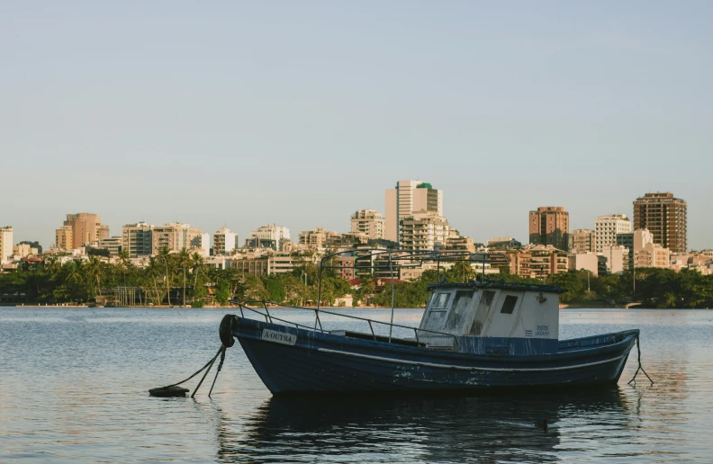 a blue boat on a body of water in front of a city