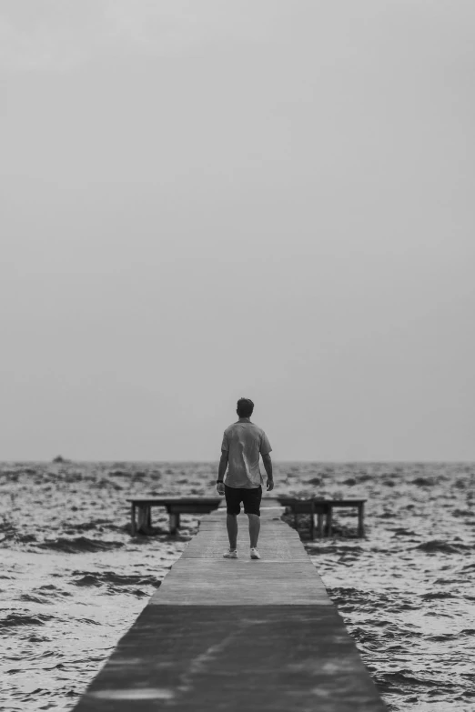 a man is walking towards the ocean on a pier