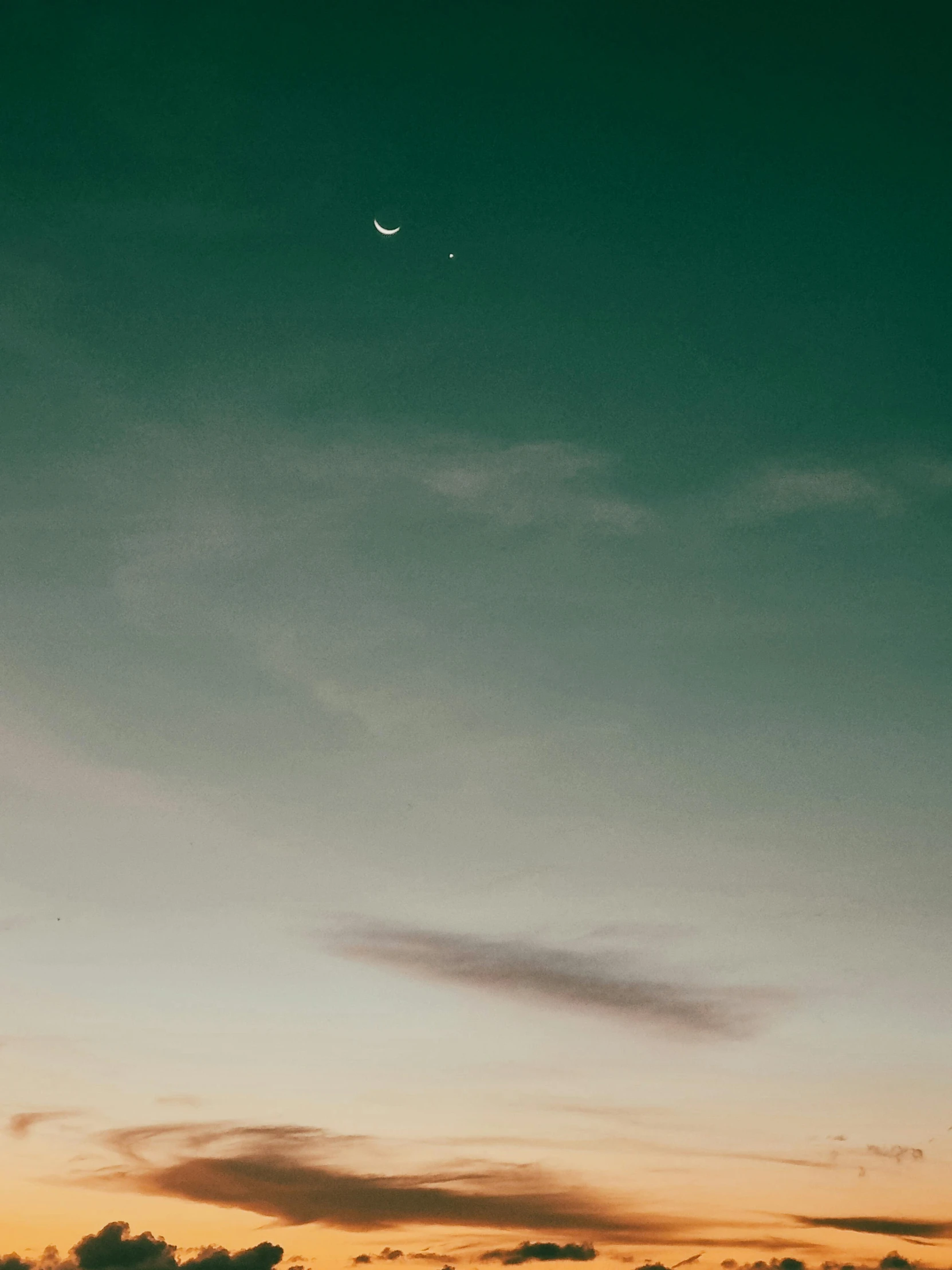 a very large hill under a cloudy sky with a moon in the distance