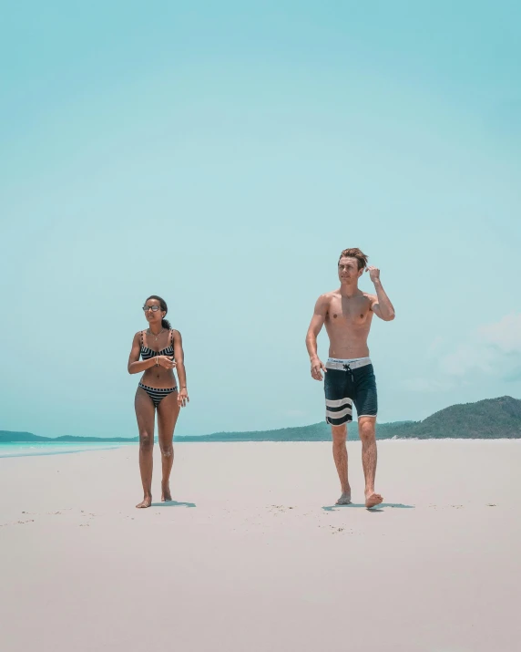 two young people in swimsuits stand in the sand at the beach