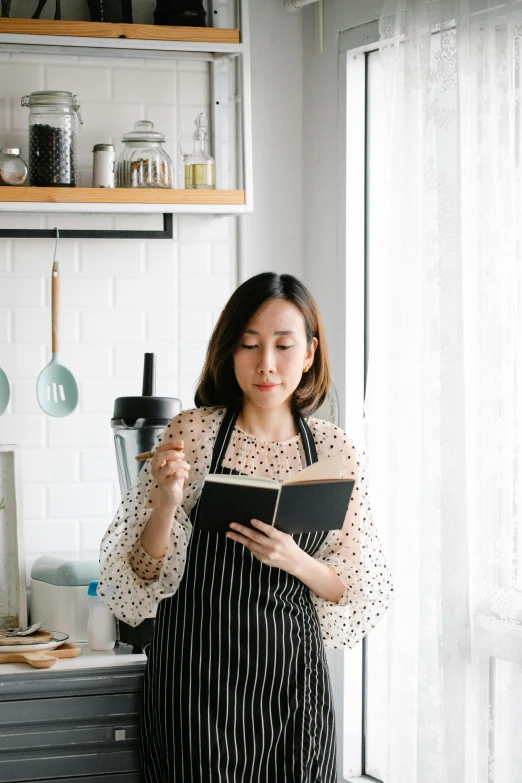 a woman standing in a kitchen holding a book