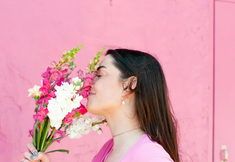 a woman smelling a bunch of flowers in front of pink background