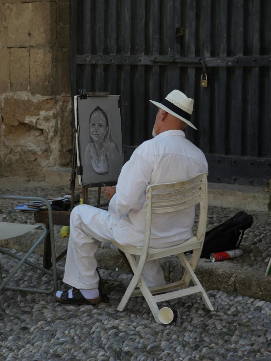 man sitting in white outfit near a painting