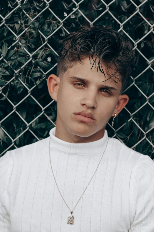 a man wearing a white sweater and standing by a fence