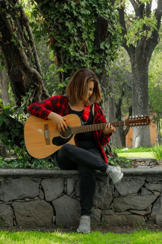 a woman with an acoustic guitar sits on a stone bench