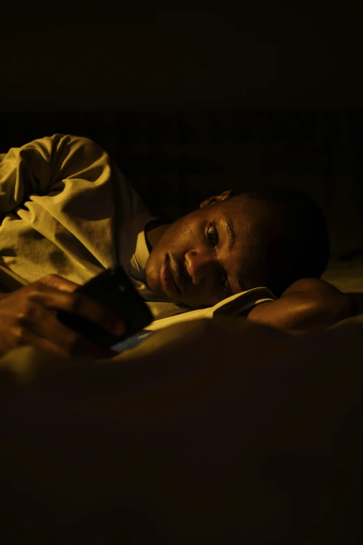 a man laying in bed under a blanket while using a cell phone