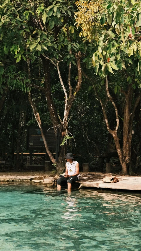 a man sitting next to the water, in front of trees