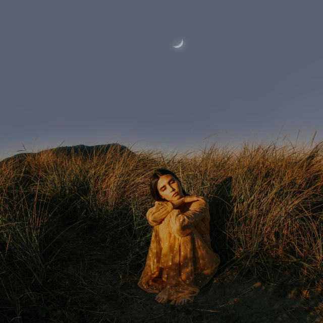 a young woman sitting in a field by the hill