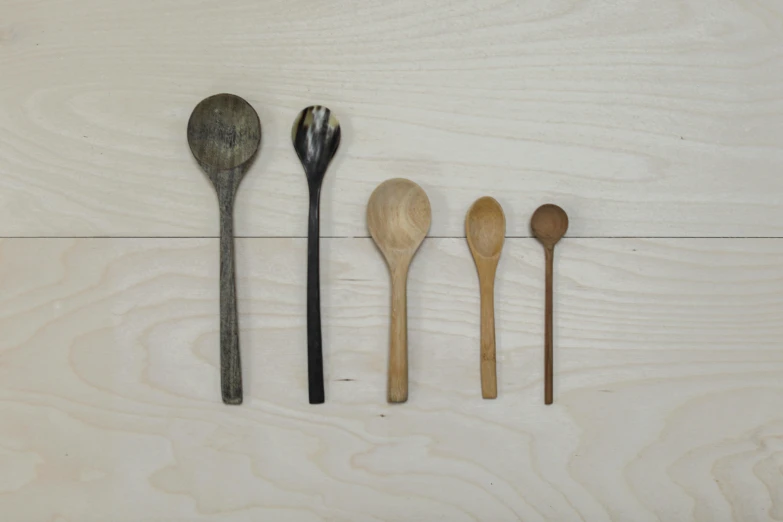 four wooden spoons in varying sizes on a white wood wall