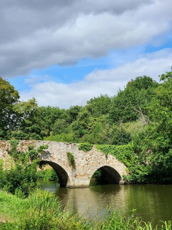 an old bridge over a river surrounded by greenery