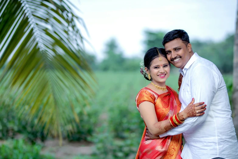 an indian couple posing for the camera with a large tree behind them