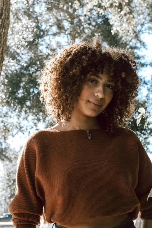 woman wearing brown sweater with curly hair posing