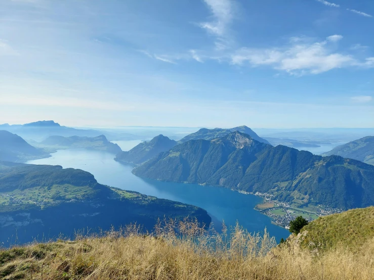 a man standing on a grassy hill with a view of some mountains and a lake