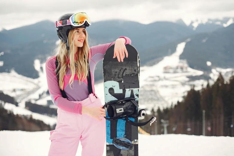 a woman posing with a snowboard at the top of a mountain