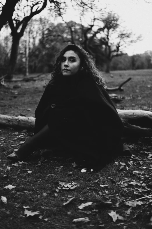 a woman is sitting on the ground in the woods