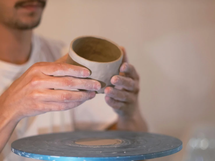 man in white shirt holding cup with two hands and making a face