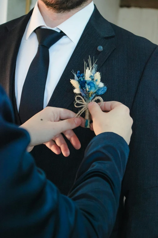 man helping woman put a boutonniere on his coat