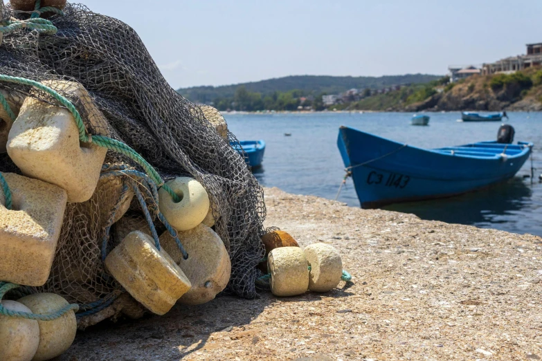 a pile of buoys on the shore with fishing boats in the distance