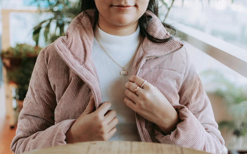 a woman in a pink jacket and a white top standing at a counter