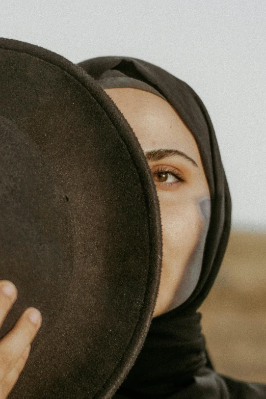 a young woman hides her face underneath a black hat