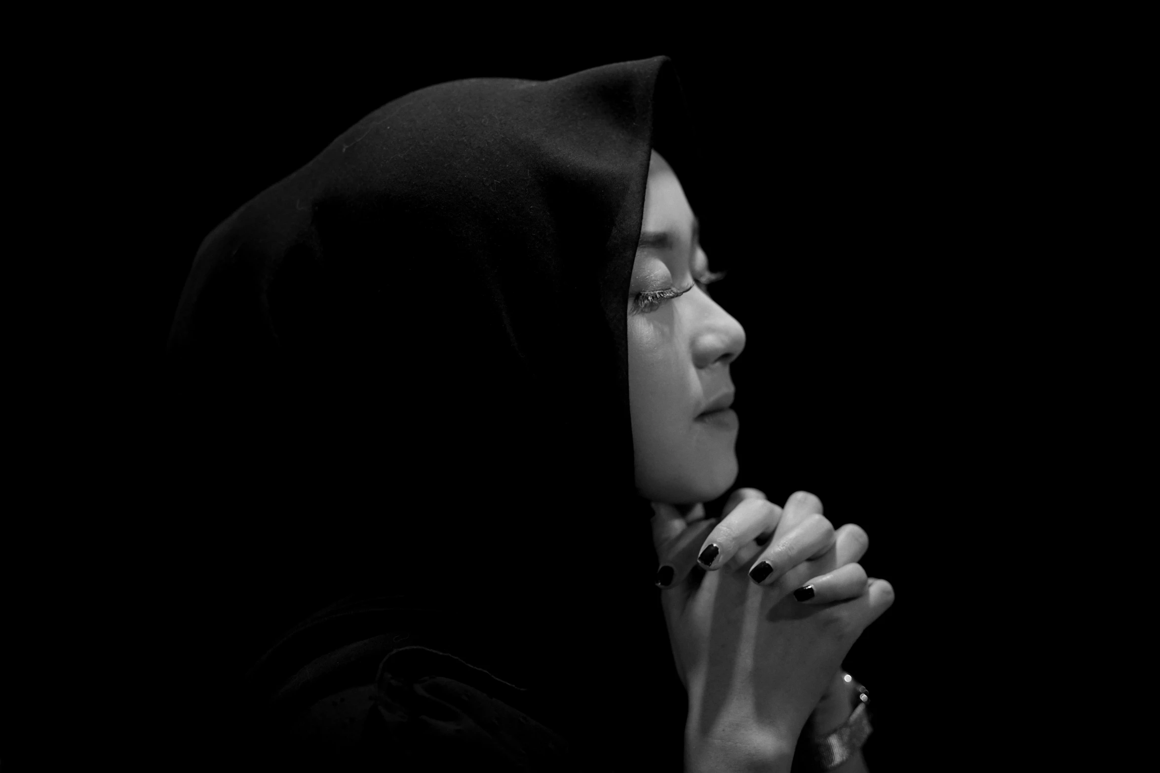 a woman wearing black praying with her hands together