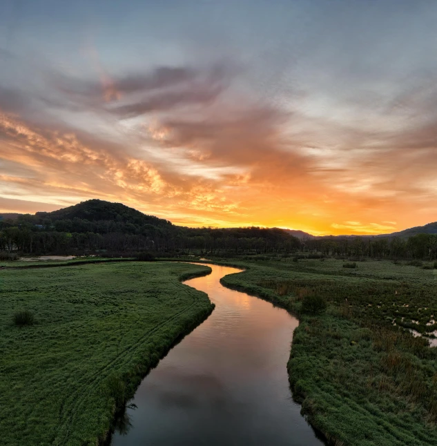 a river runs through a lush green field with mountains in the background