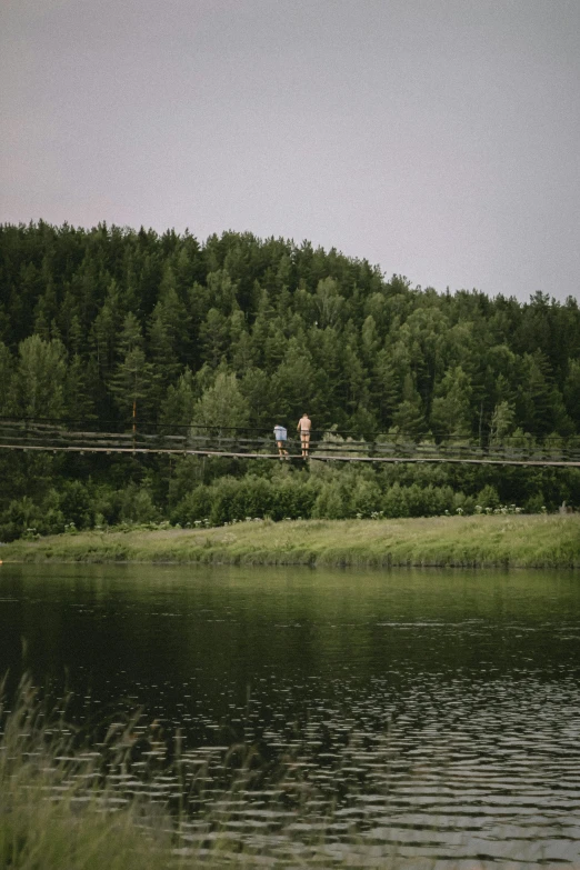 a lake with two people walking in the distance and trees on the other side