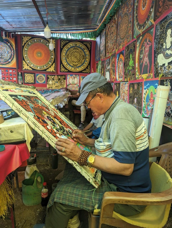 the older man is sitting down with his colorful tapestry