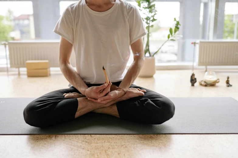 a man in a white t - shirt sitting in a yoga pose on a blue mat