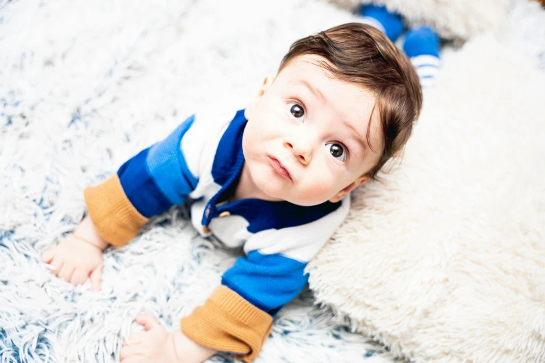 an adorable toddler looking up while lying on a white sheepskin rug