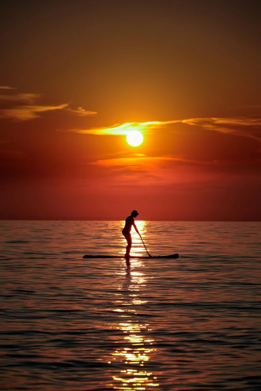 the person is standing on surf board at sunset