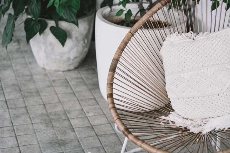 rattan chair on grey tiled floor next to potted plants