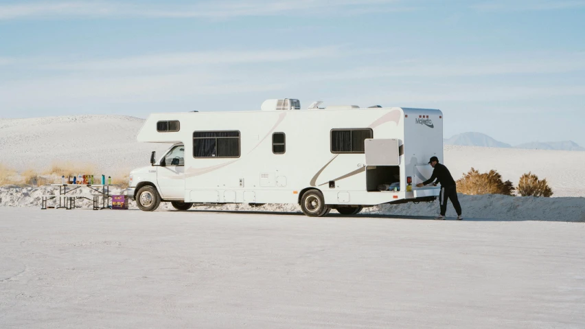 a man standing next to an rv parked on the sand