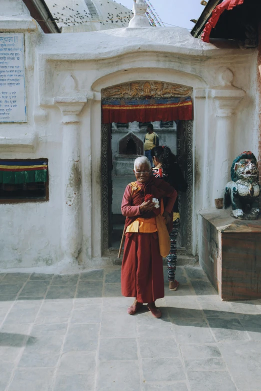 an old man in a red robe standing in front of a building