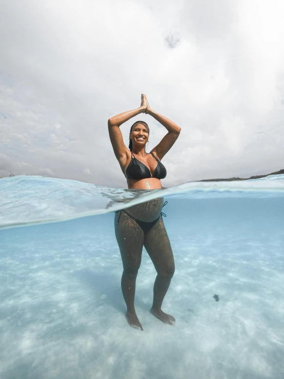 a woman in black bikini posing in water with bottle above her head