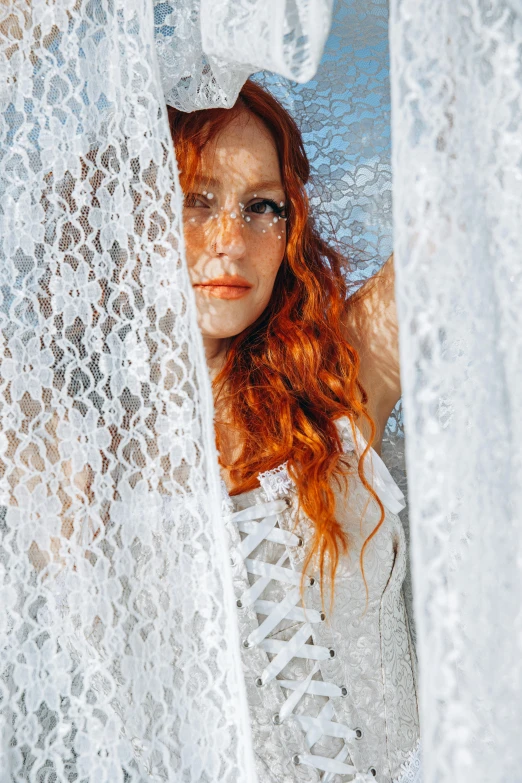 woman standing behind sheer curtains looking out the window