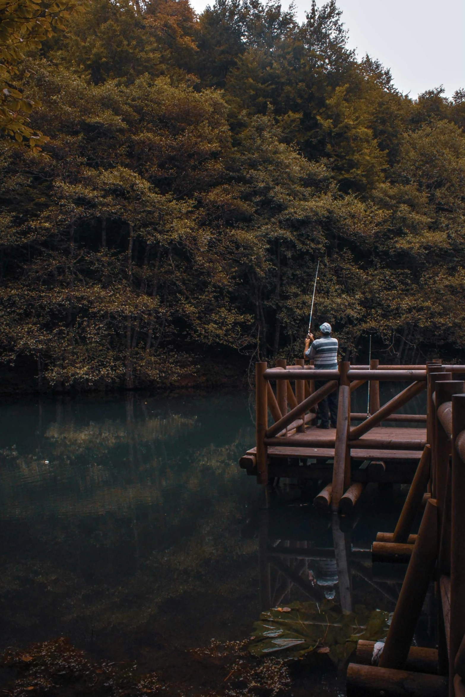 man on dock with fishing pole next to wooded area