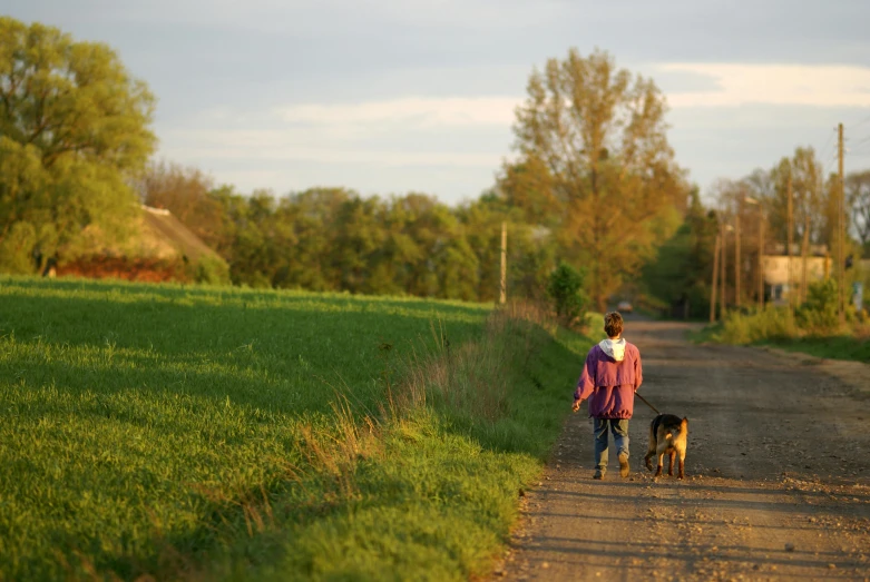a woman and her dog walk along a dirt road