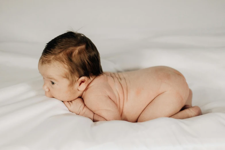 baby laying down on white sheets looking at the camera