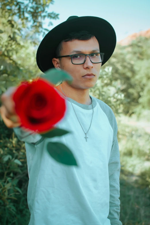 a young man with glasses and a hat holding a red rose