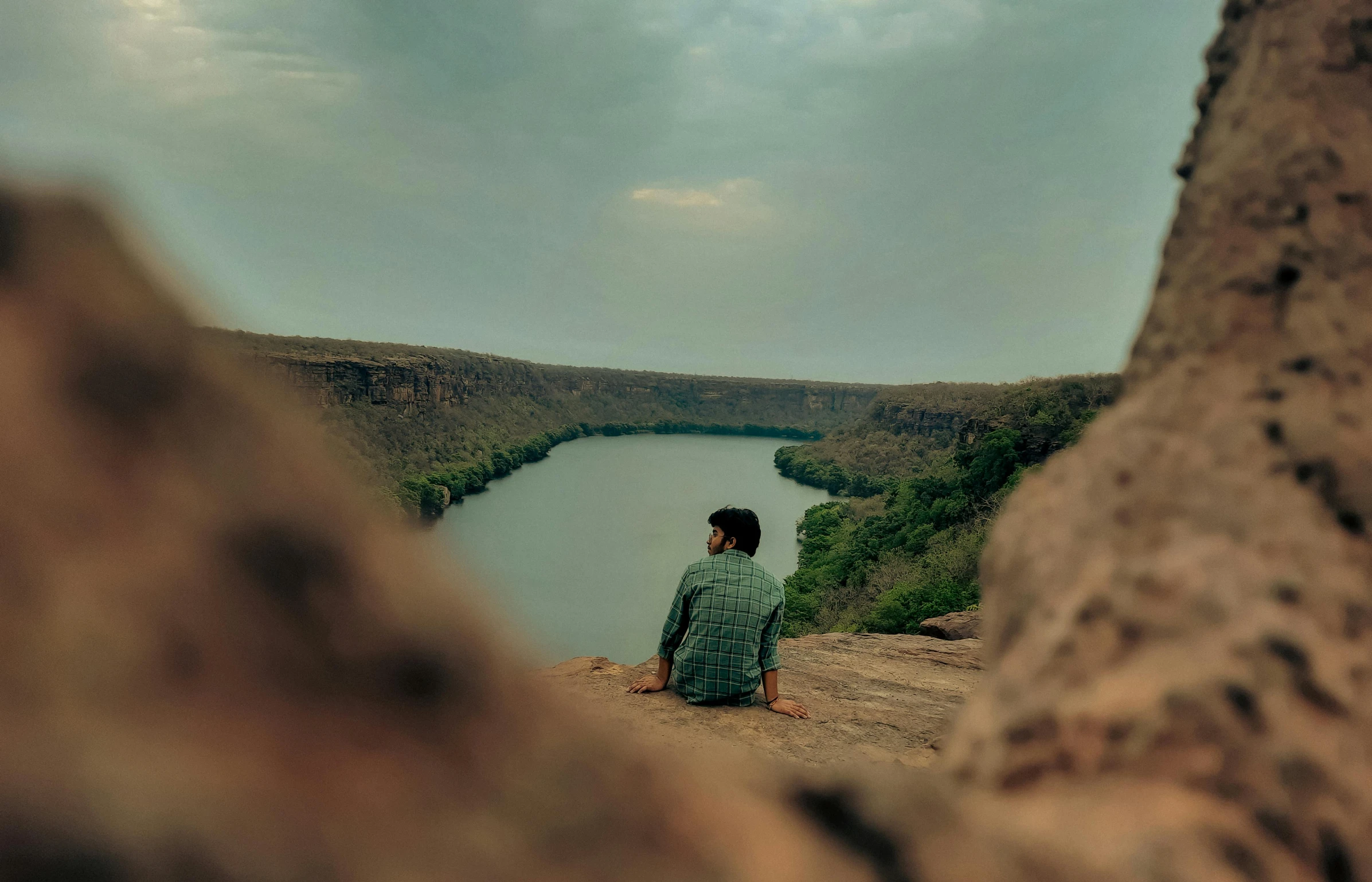 a man sitting on top of a rocky cliff next to a lake