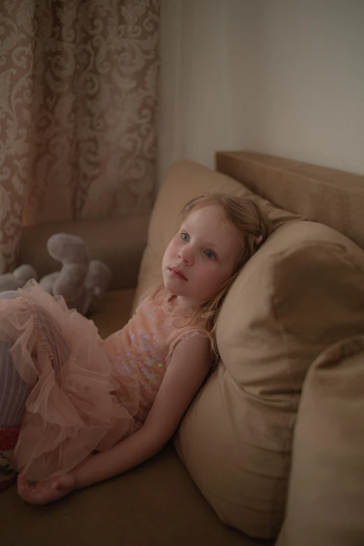 a little girl laying on top of a brown couch