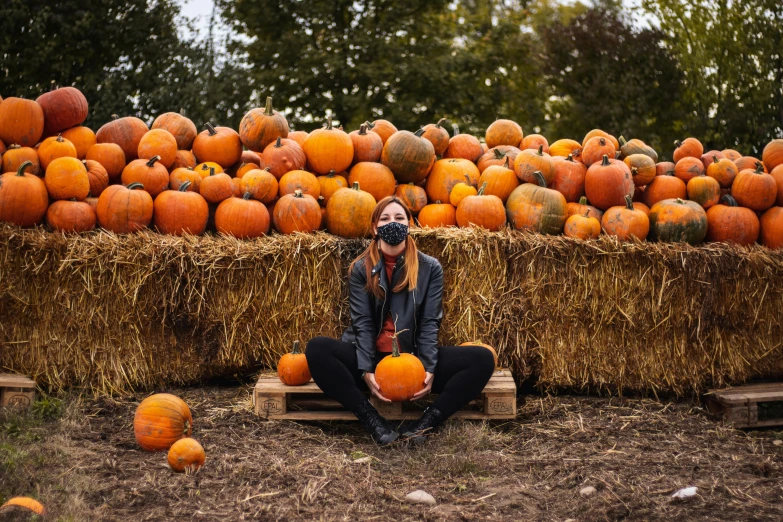 a person wearing a mask sitting near hay bales